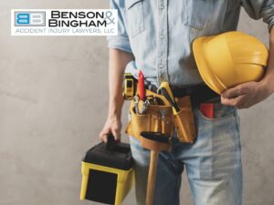 A construction worker holding a yellow hard hat and a portable toolbox, with a tool belt around their waist, representing the use of Personal Protective Equipment