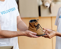 Volunteer Handing Pair Of Kid's Boots To Young Teen